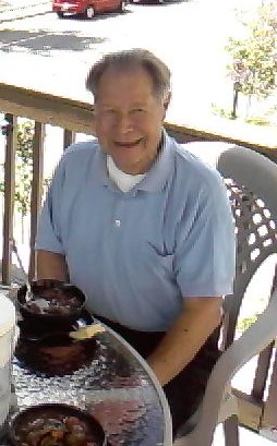 The Legacy That Guides Us Smiling elderly man sitting at a table with bowls on a porch.